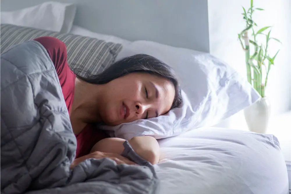 Woman sleeps under weighted blanket in bright bedroom