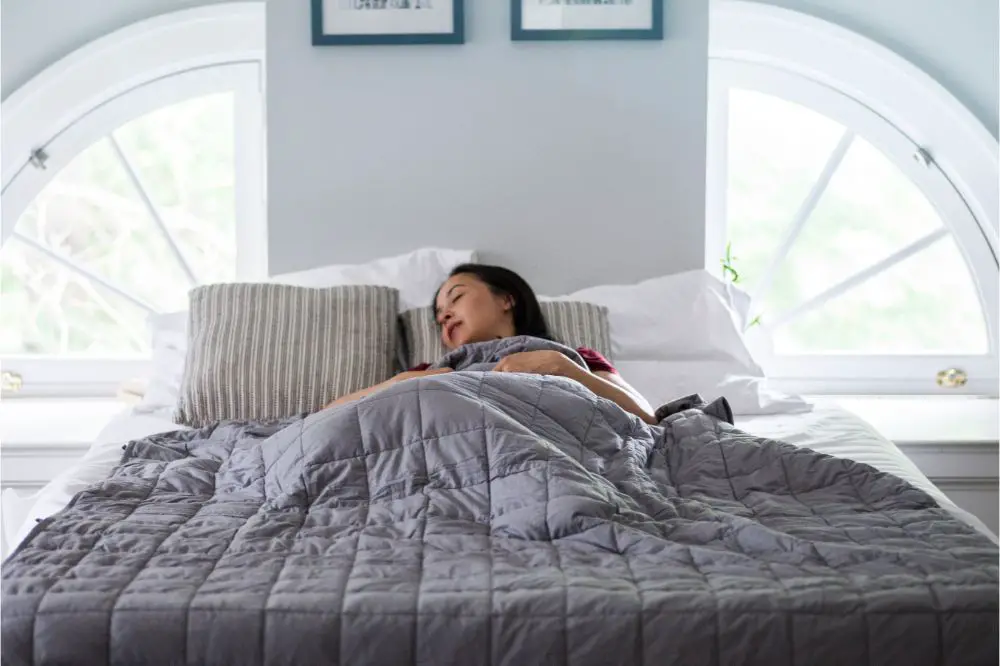 Woman sleeps under weighted blanket in bright bedroom