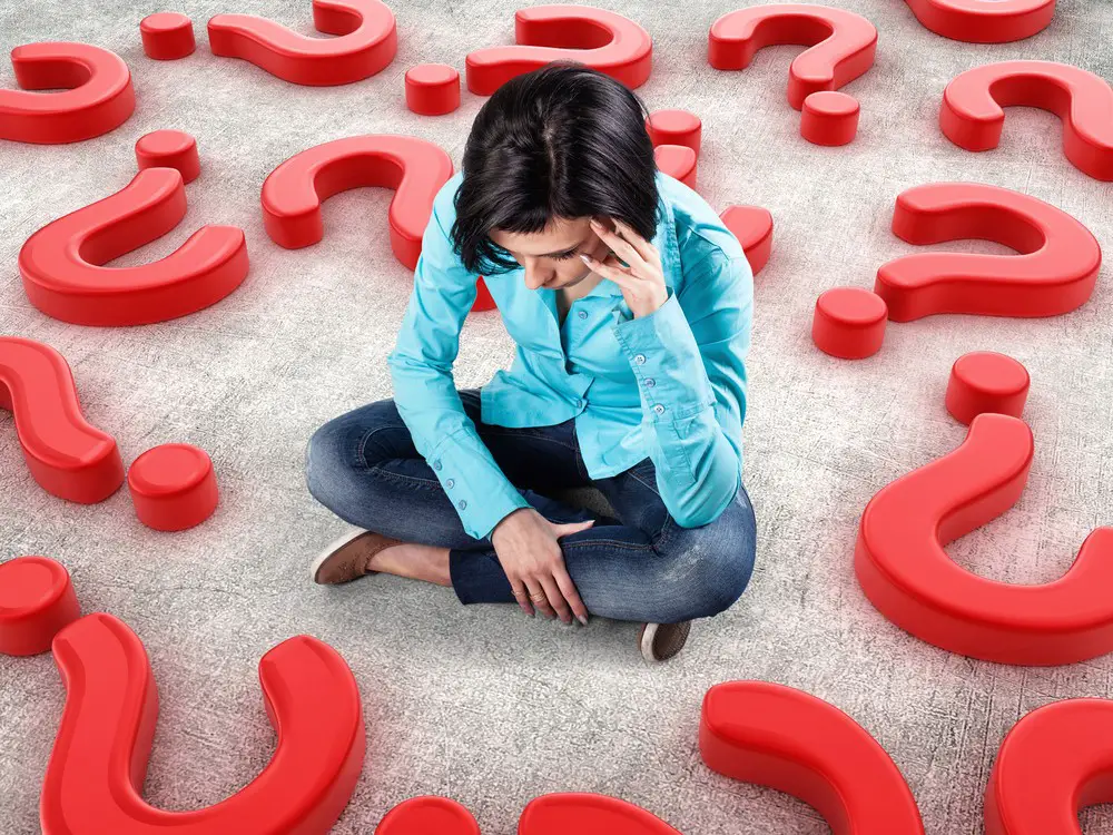 Sad girl sits among many red questions